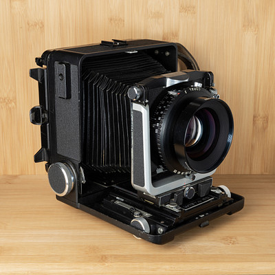 The image features a vintage camera sitting on top of a wooden table. The camera is black and white, with its lens facing the viewer. It appears to be an old-fashioned model, possibly a Polaroid or a similar type of camera.