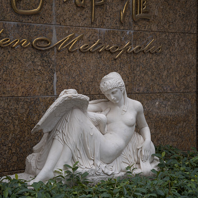 The image features a statue of a woman sitting on the ground, holding an open book. She appears to be reading or resting with her legs crossed. The statue is made of marble and has a white color.