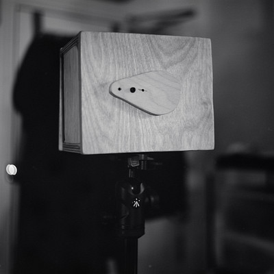 The image is a black and white photo of an old wooden box with a camera on top. The box appears to be made from wood, possibly plywood or another type of wood. It has a vintage look, giving the impression that it was taken many years ago.