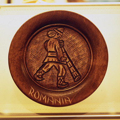 The image features a wooden coin with an intricate design on it. The coin is shaped like a man and has the word "Romania" written in Romanian letters. It appears to be a unique piece of art or decoration, possibly made from wood or another material.