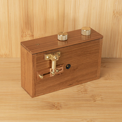 The image features a wooden box with two knobs on the top. One of the knobs is located towards the left side, while the other one is situated more towards the center. The box appears to be made from wood and has a brown color.
