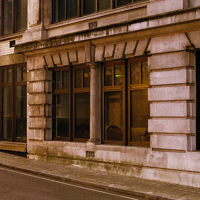 The image features a large, old building with many windows. It appears to be an office or commercial space, as there are several chairs visible in the scene. Some of these chairs can be seen near the center of the building, while others are located closer to the right side.