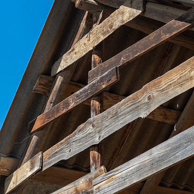 The image features a wooden structure with a rustic appearance, possibly an old barn or shed. It has a sloped roof and is made of wood planks that are visible in the foreground. The sky can be seen through the gaps between the wooden slats, creating a sense of openness and natural light.