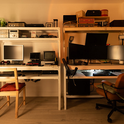 The image features a well-organized home office with various electronic devices and equipment. There is a desk with two computers, one on the left side of the room and another towards the right. A chair can be seen placed in front of each computer, providing comfortable seating for users.