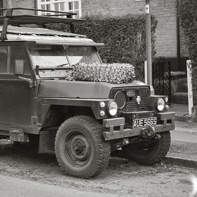 The image is a black and white photo of an old truck parked on the side of a street. The truck has a flatbed, and it appears to be carrying some items in its bed. There are several bananas visible in the back of the truck, as well as a few apples.