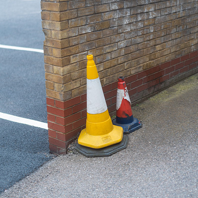 The image features a sidewalk with two brightly colored traffic cones placed on the ground. One of the cones is yellow, while the other one is red and white. They are positioned close to each other, creating an eye-catching display.