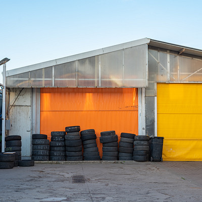 The image features a large garage with an orange roof, which is filled with numerous tires. There are at least 14 tires of various sizes and types piled up inside the garage. Some of these tires are stacked on top of each other, while others are placed side by side or in smaller groups.