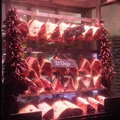 The image features a display case filled with various types of meat, including ribs and steaks. The meats are arranged in an appealing manner on shelves, showcasing their freshness and quality. There is also a sign hanging above the display case, likely providing information about the products or prices.