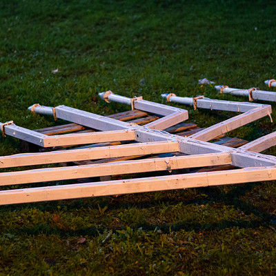 The image features a large number of wooden planks arranged in an odd shape, possibly for a project or artistic display. These planks are scattered across the grassy area, with some placed horizontally and others vertically. In total, there are 13 visible wooden planks, each varying in size and position.