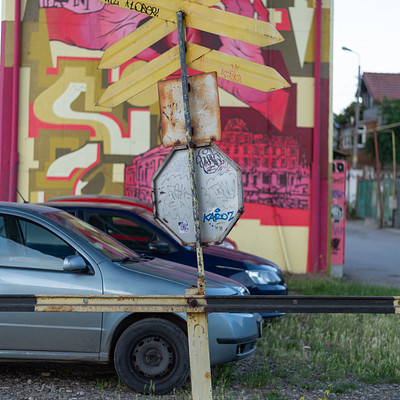 The image features a street scene with two cars parked next to each other. One car is on the left side of the frame, while the other is positioned further back and slightly to the right. A stop sign can be seen in the middle of the scene, possibly indicating an intersection or a point where drivers need to stop.