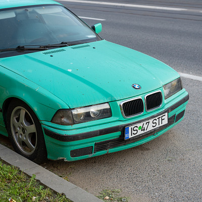 The image features a bright blue BMW car parked on the side of a road. The car is positioned near the curb, and it appears to be in good condition despite its vibrant color. There are no other cars visible in the scene, making this particular vehicle stand out from the surroundings.