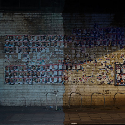 The image is a black and white photo of a brick wall with many pictures posted on it. There are several bicycles parked in front of the wall, creating an interesting contrast between the old-fashioned brick building and modern transportation. In addition to the bikes, there are also two benches visible in the scene, one located near the left side of the image and another towards the right.