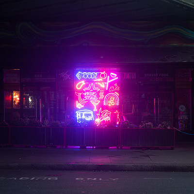 The image is a black and white photo of a neon sign on the side of a building. The sign appears to be advertising something, possibly related to food or entertainment. There are several potted plants placed around the area, adding some greenery to the scene.