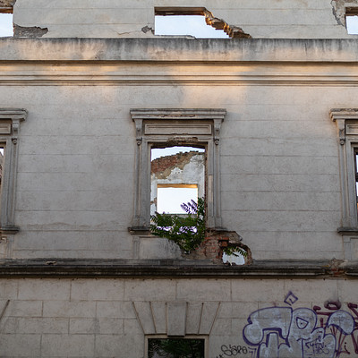 The image features a building with four windows on each side, all of which are boarded up. The windows have graffiti written on them, adding an urban and artistic touch to the scene. The building appears to be in a state of disrepair or under construction, as indicated by the broken window panes.
